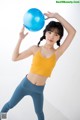 A woman in a yellow top and blue leggings holding a blue ball.