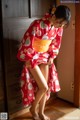 A woman in a red kimono standing on a wooden floor.