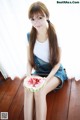 A woman sitting on a wooden floor holding a slice of watermelon.