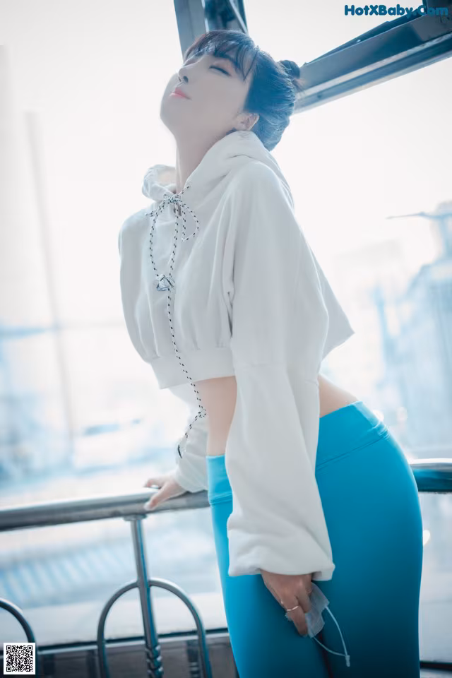 A woman in a white shirt and blue pants leaning against a railing.
