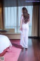 A woman in a white dress standing in a hotel room.