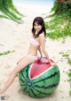 A woman in a bikini sitting on a watermelon on the beach.